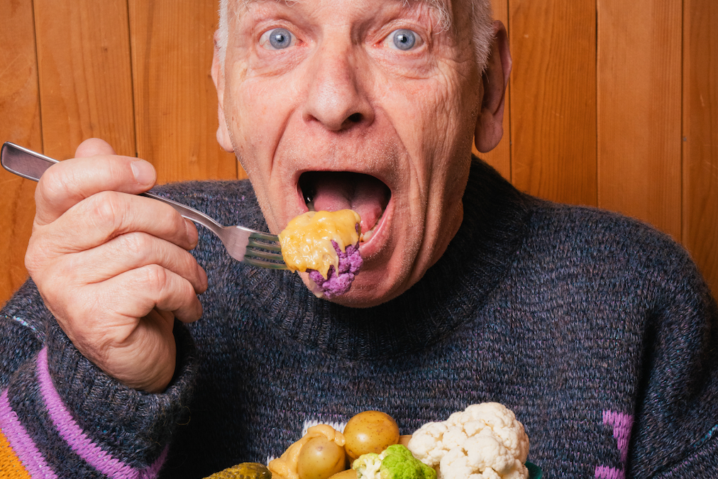 Man eating a plate of vegetables covered in Vegan Raclette with a surprised and excited expression